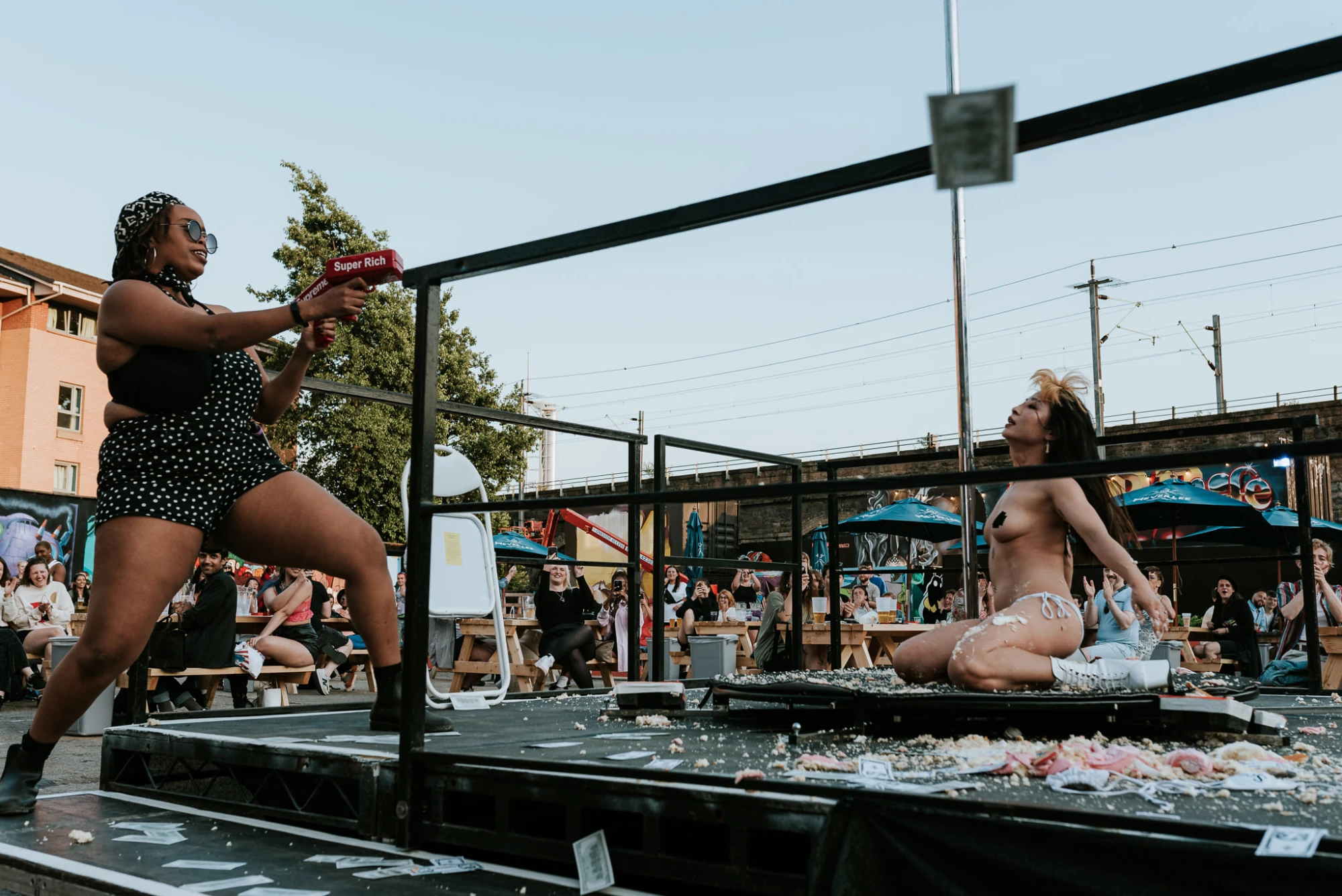a woman sat on a cake while another woman shot money at her out of a gun.