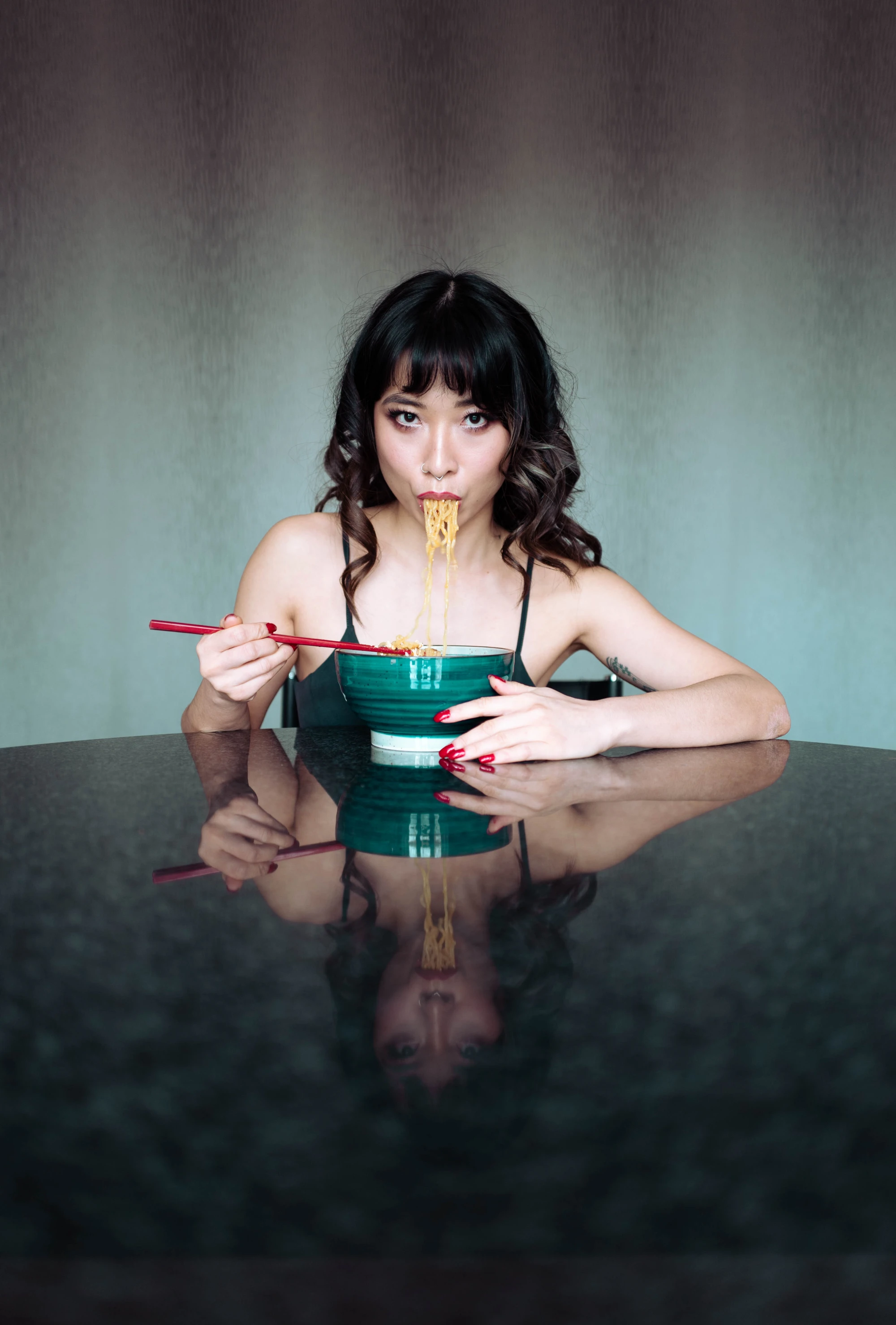 a chinese woman holds noodles in her mouth as she stares at the camera.