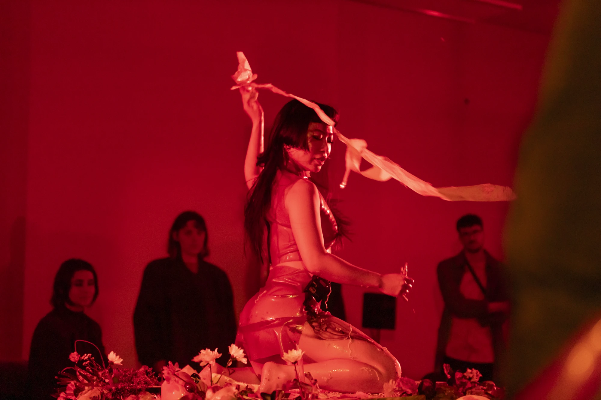 performance documentation of a woman throwing a ribbon of paper. There is a wash of red light.