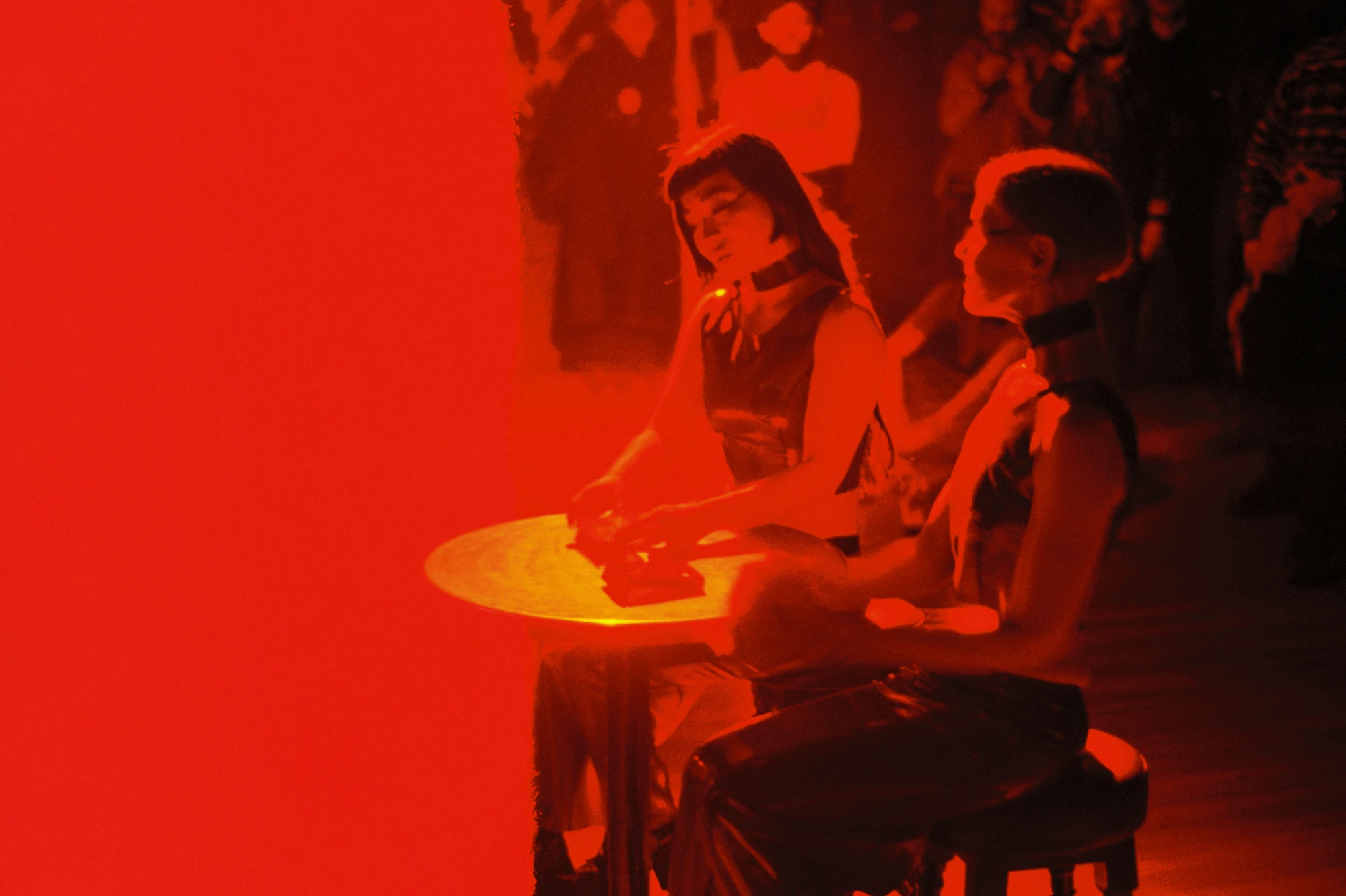 two people sit at a table, whilst an audience looks on.