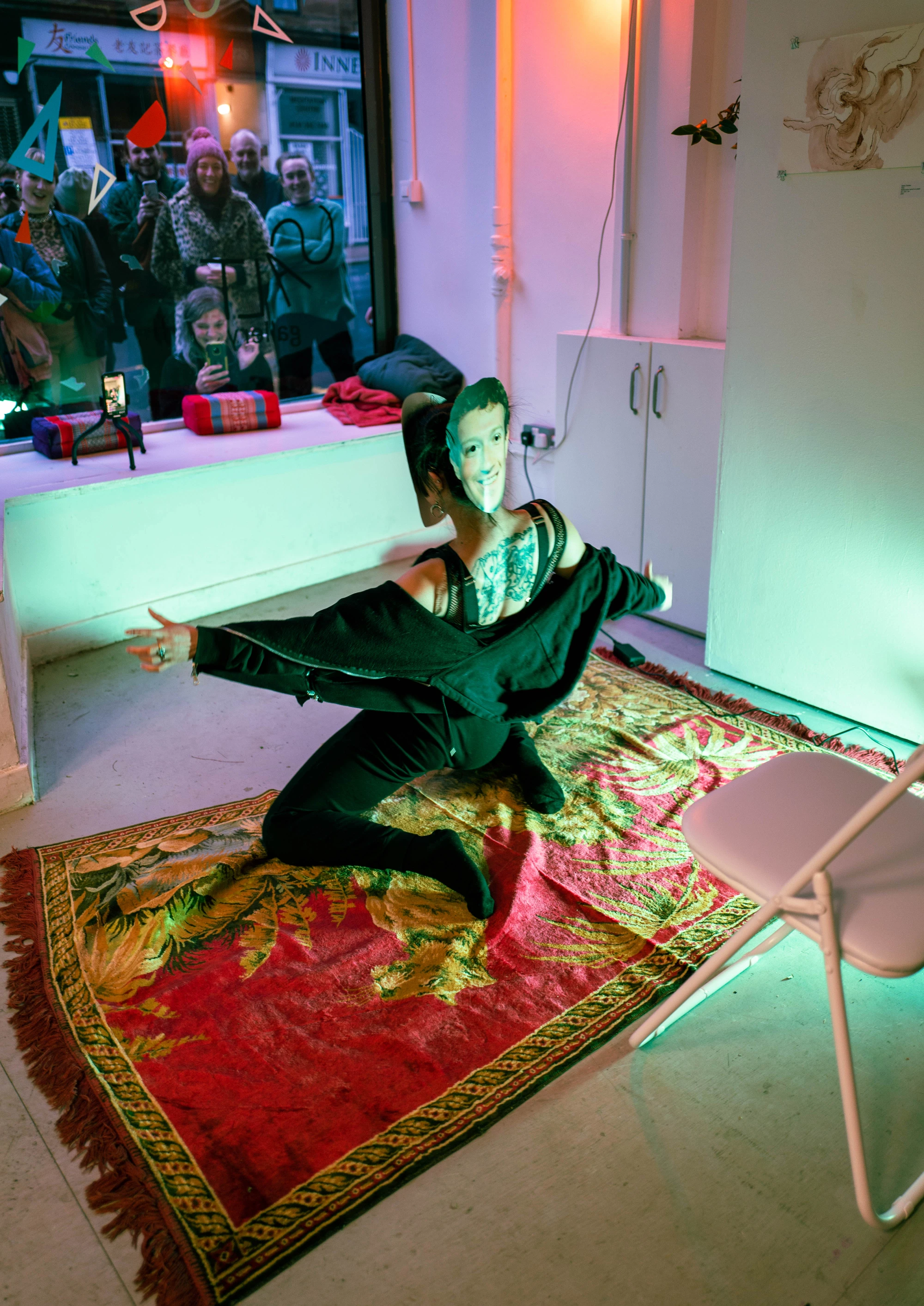 a woman wearing black hoodie and sweatpants performs as Mark Zuckerberg. The audiences watches through the shopfront window.