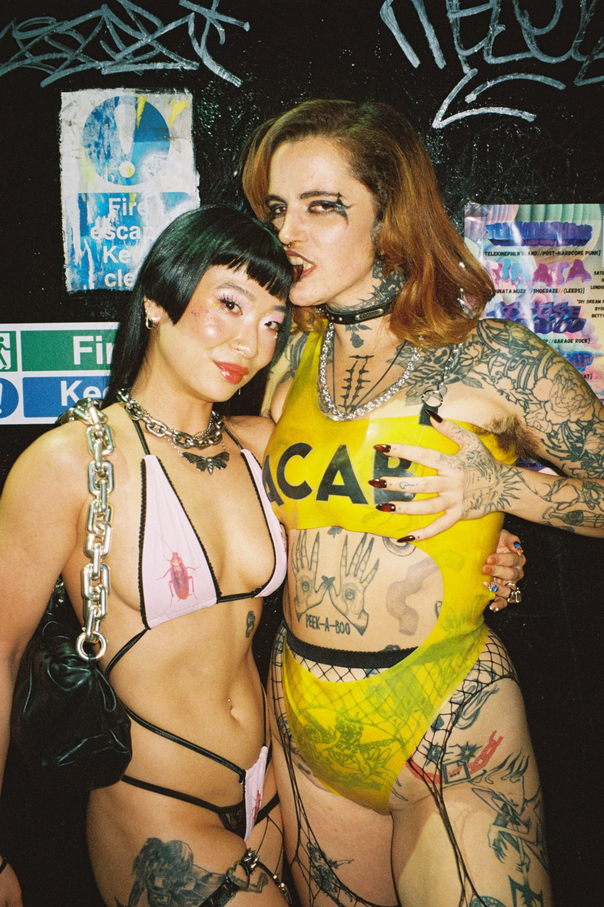 two women stand outside a nightclub wearing very little clothes.