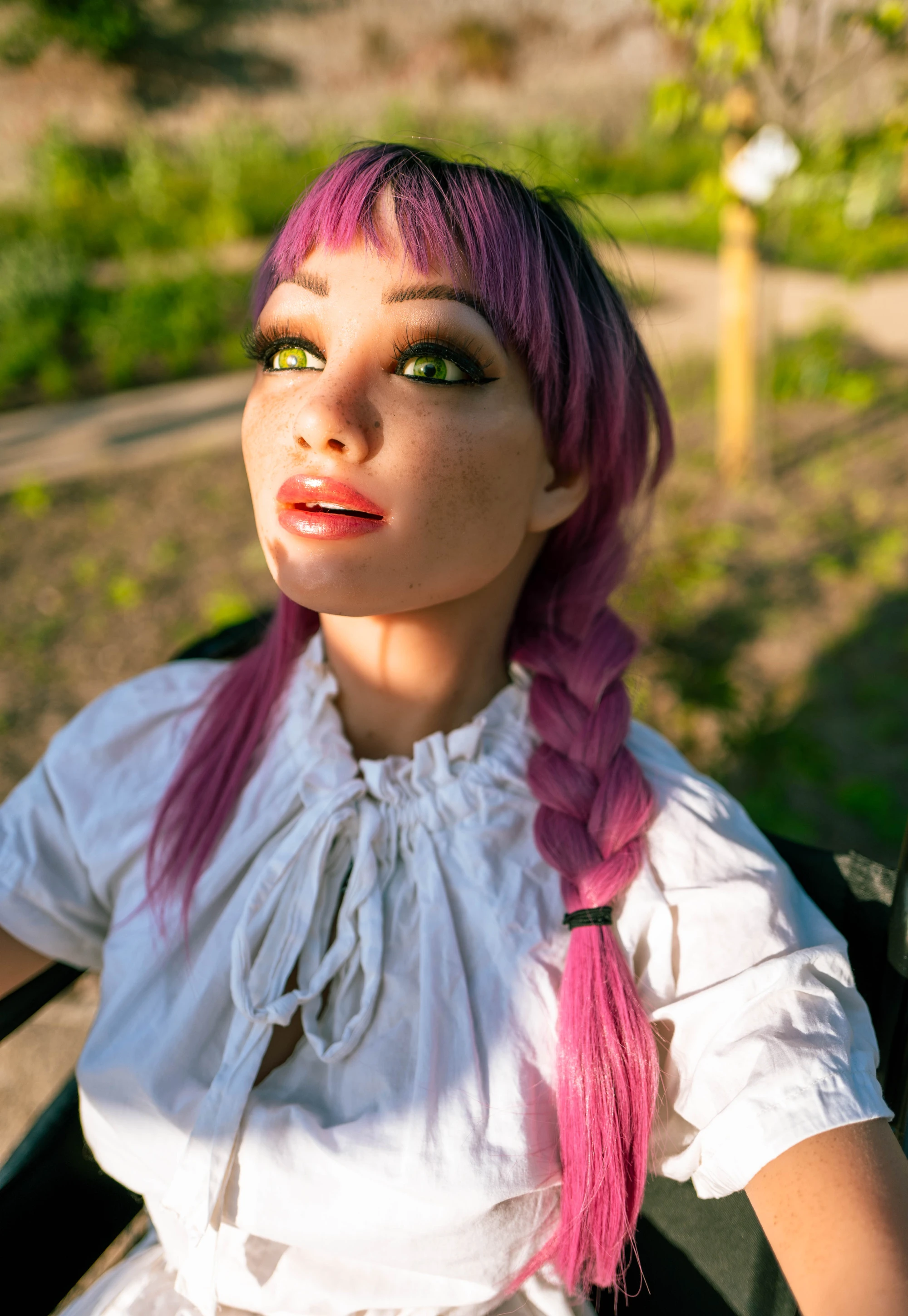 a silicone love doll looks upwards, the sun caught in her green eyes.