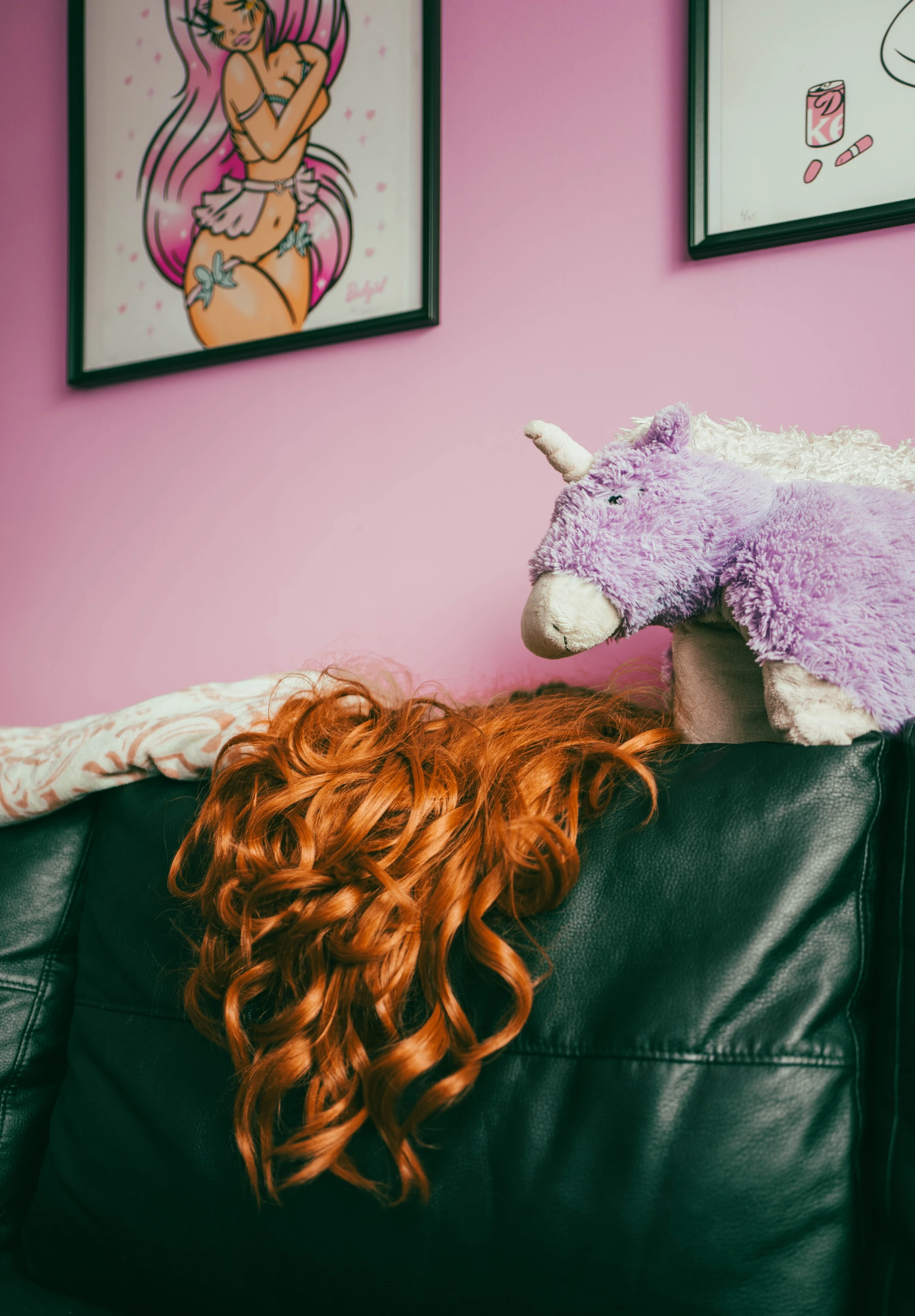 a red wig rests on top of a leather sofa, with a purple unicorn next to it.